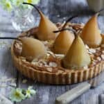 A French almond tart with whole poached pears sitting on a gray background.
