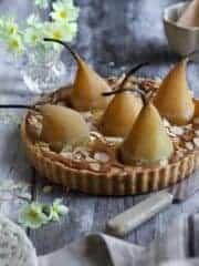 A French almond tart with whole poached pears sitting on a gray background.