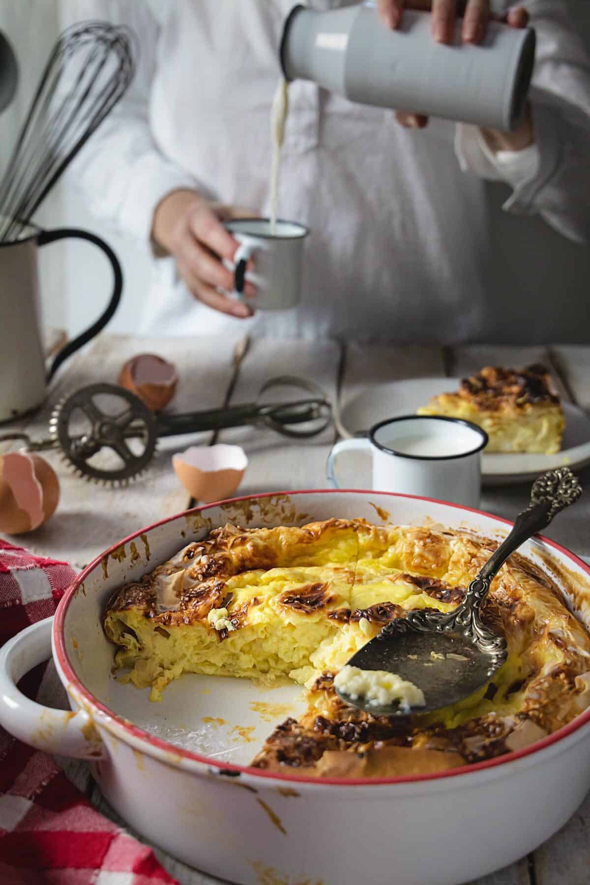 A close up of the partial egg pie with person pouring milk into a cup in the background.