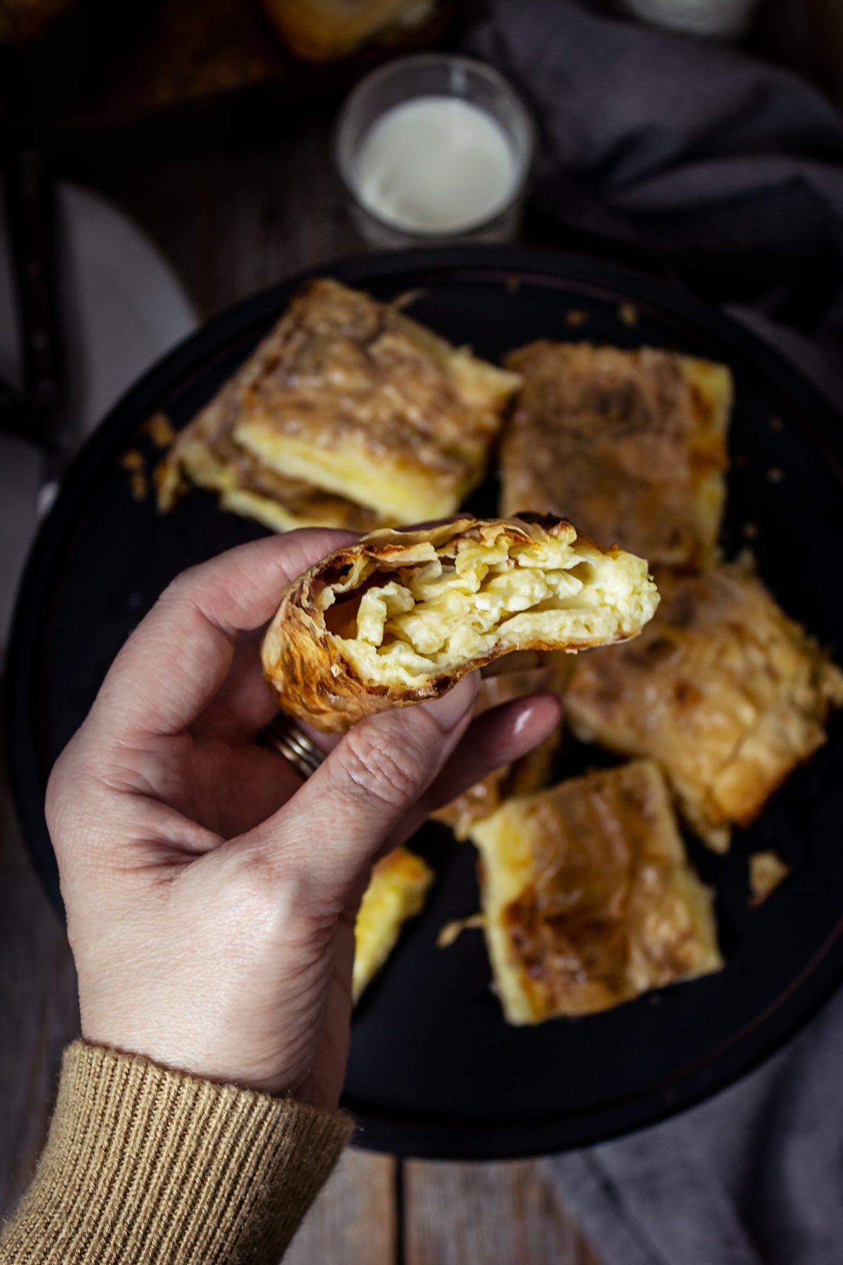 A person holding a piece of fillo cheese pie in a hand showing the filling inside.