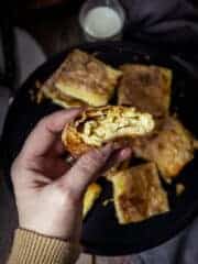 A person holding a piece of fillo cheese pie in a hand showing the filling inside.