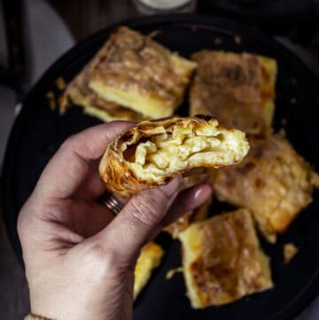 A person holding a piece of fillo cheese pie in a hand showing the filling inside.