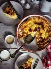 Round baking dish with fillo egg pie and two slices on plates sitting on a wooden white table.