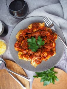 Italian ragu over pasta on a plate with wine glasses.