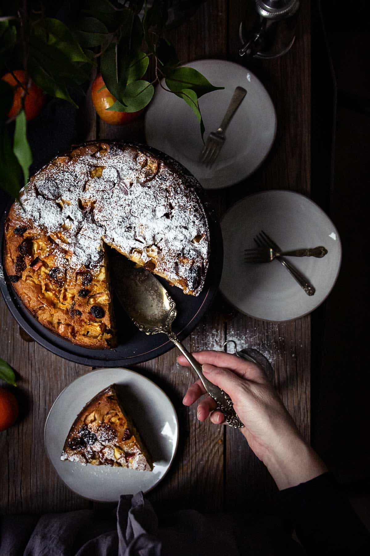 An overhead shot of the apple polenta cake with one slice removed and person serving it.