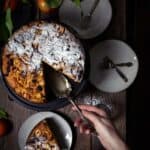 An overhead shot of the apple polenta cake with one slice removed and person serving it.