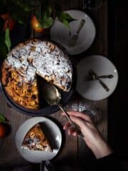 An overhead shot of the apple polenta cake with one slice removed and person serving it.