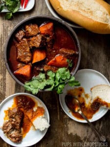 Bo Kho stew in a bowl with beef and carrot chunks surrounded with plates and bread.