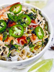 A bowl with chicken and shrimp pho soup with vegetables and noodles.