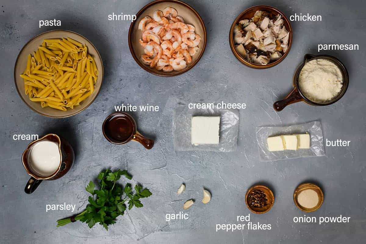 Ingredients for the pasta alfredo on the table with cream cheese, garlic, cooked chicken, and shrimp.