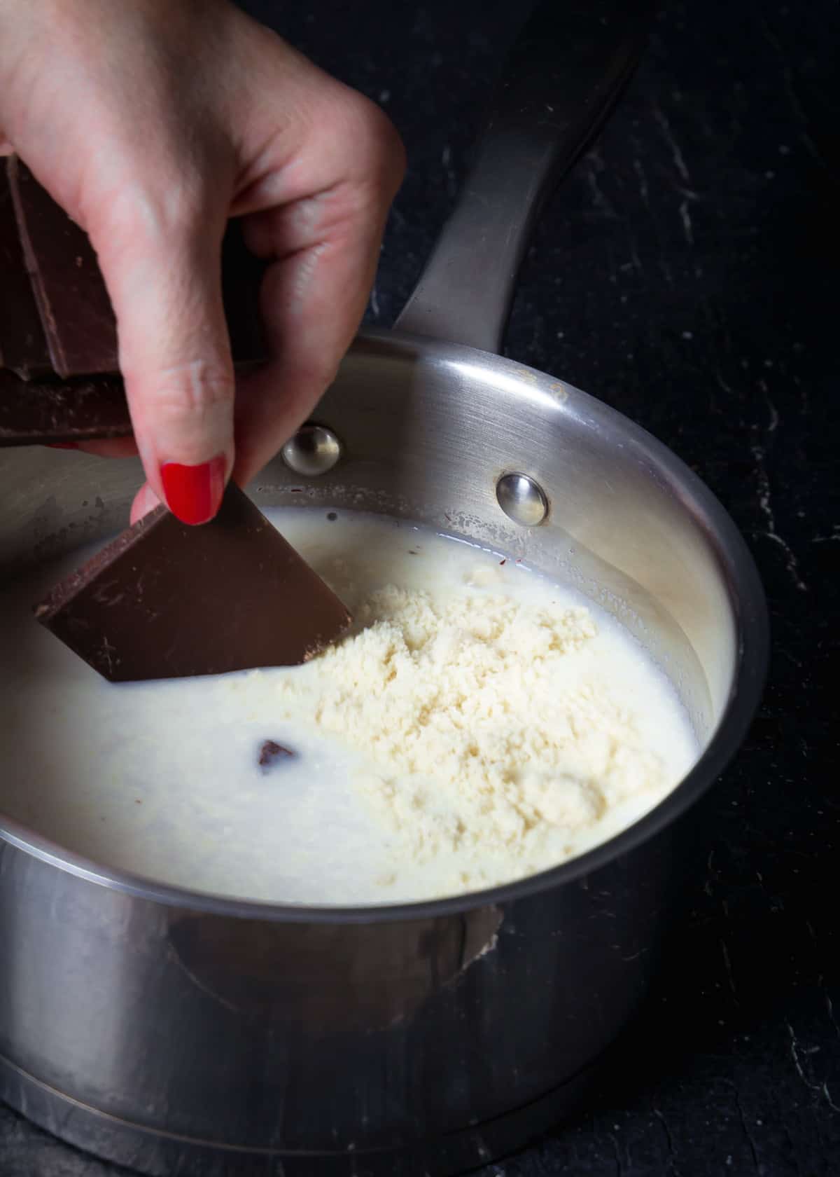 Adding chocolate to the milk with almond meal in a pot.