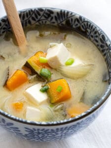A bowl of miso soup with chicken and tofu.