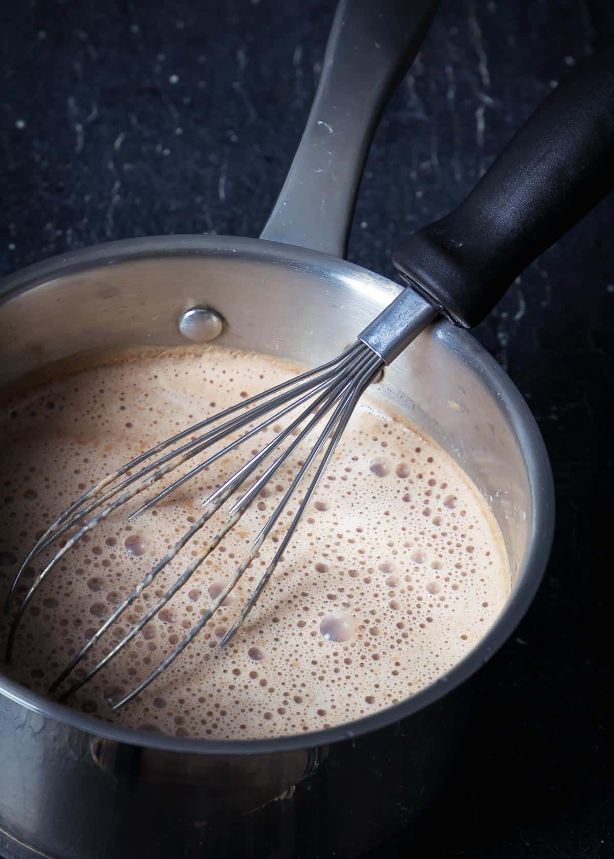A pot with all ingredients for xocolatl and a whisk on the stove.
