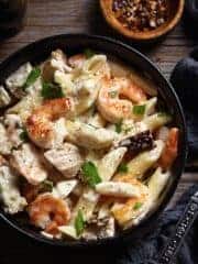 A close up of creamy penne Alfredo with chicken and shrimp in a bowl.