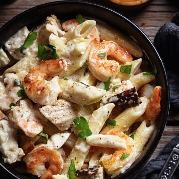 A close up of creamy penne Alfredo with chicken and shrimp in a bowl.
