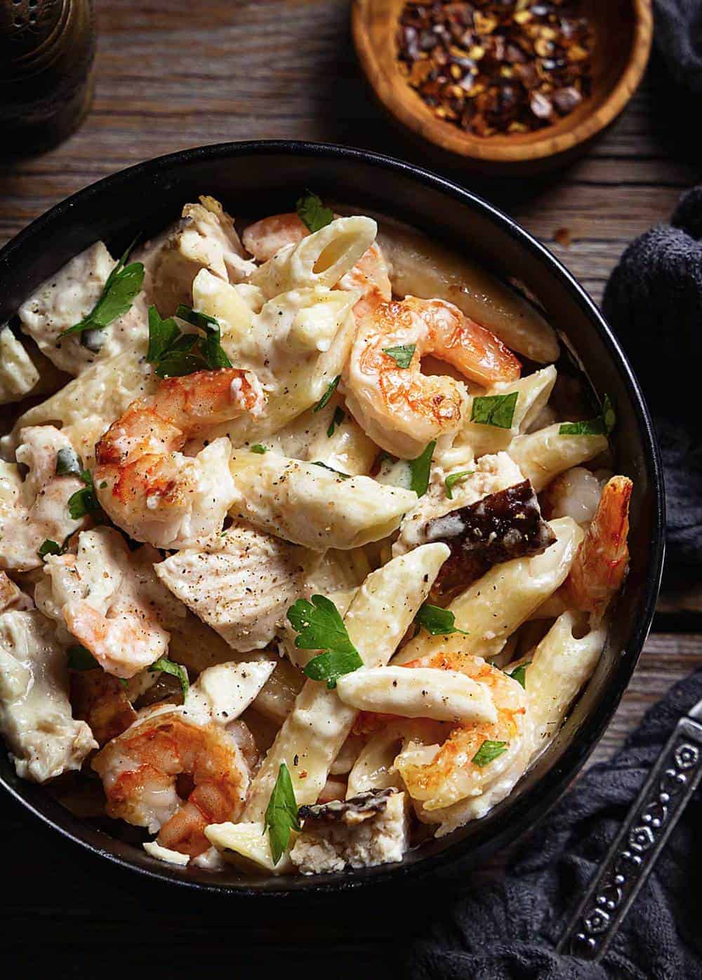 A close up of creamy penne Alfredo with chicken and shrimp in a bowl.