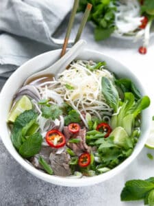 A bowl of pho with vegetables, beef, and noodles.