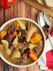 A bowl of soup with chunks of beef and pumpkin on a table.
