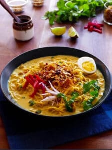 A bowl of Burmese noodle dish with boiled egg half, peppers, onions, and parsley.