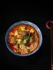 A bowl of ramen soup with beef on a black background.