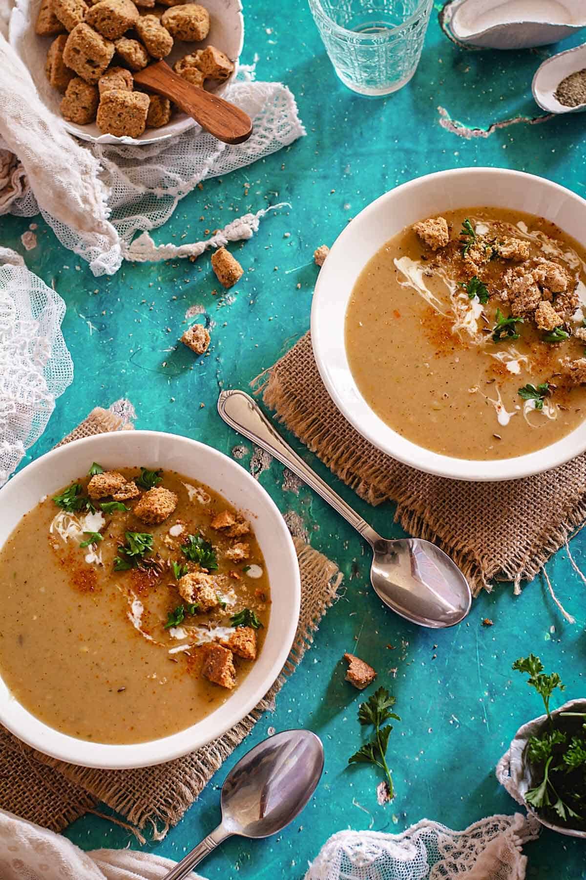 Two shallow bowls with roux soup topped with croutons on a green table with utensils.