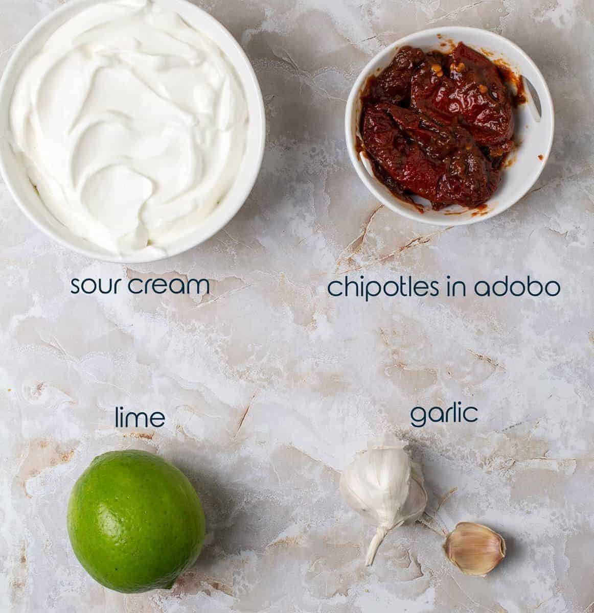 Four ingredients for chipotle sauce with sour cream, garlic, lime, and adobo peppers.