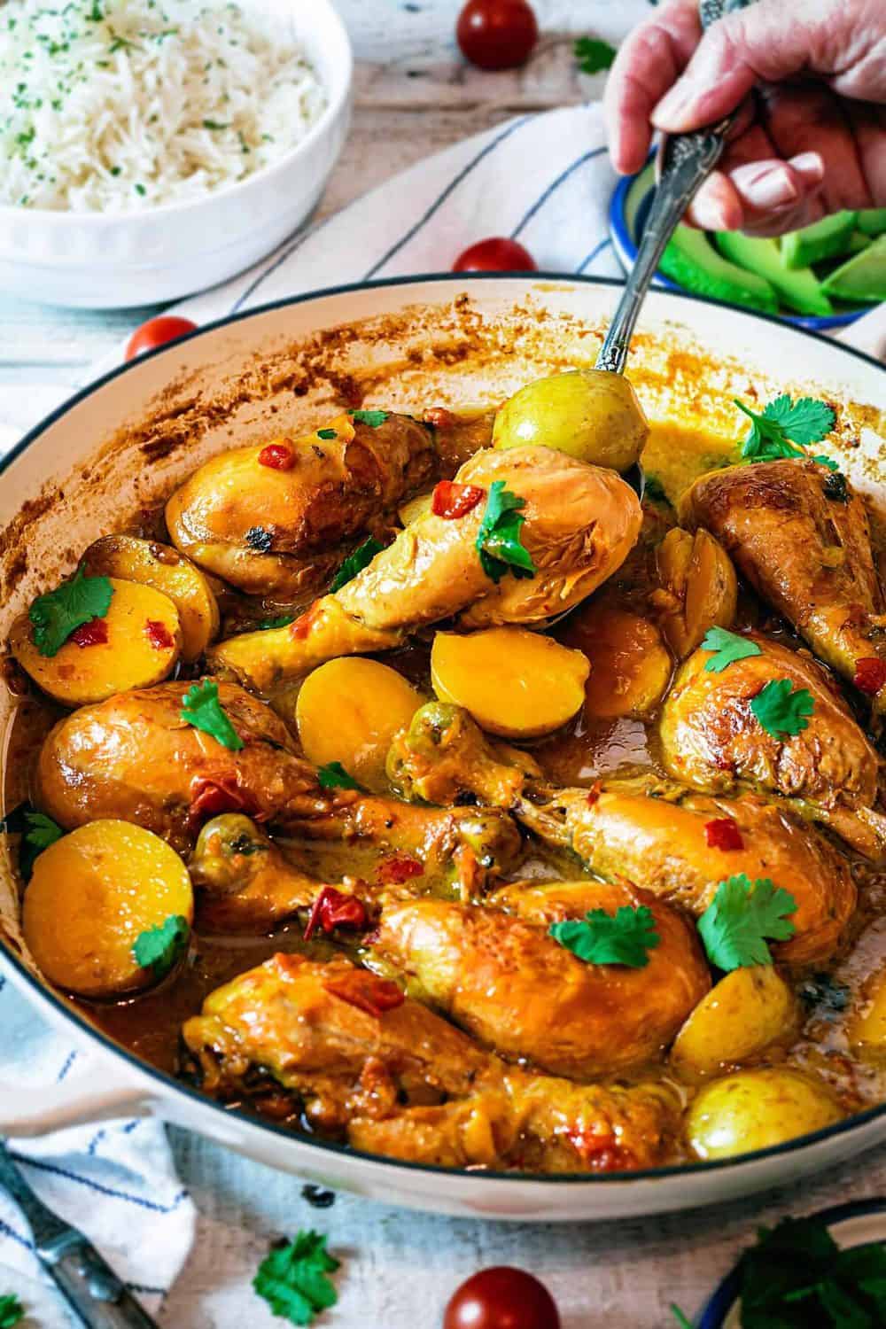 A person digging into the chicken and potato stew with a spoon. 