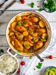 Colombian stew with chicken and potatoes in a Dutch oven on a white wooden table with other condiments.