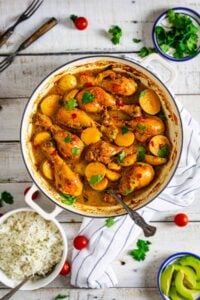 Colombian stew with chicken and potatoes in a Dutch oven on a white wooden table with other condiments.