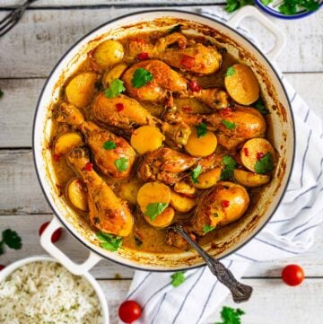 Colombian stew with chicken and potatoes in a Dutch oven on a white wooden table with other condiments.