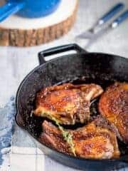 A cast-iron skillet with pork chops glazed with honey on a table.