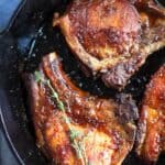 Close up of browned pork chops in a skillet with thyme twig.