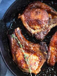 Close up of browned pork chops in a skillet with thyme twig.