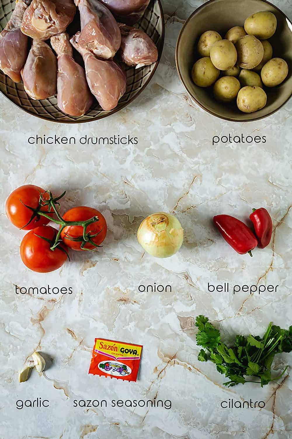 Ingredients for Sudado de Pollo with chicken drumsticks, potatoes, tomatoes, and seasonings.