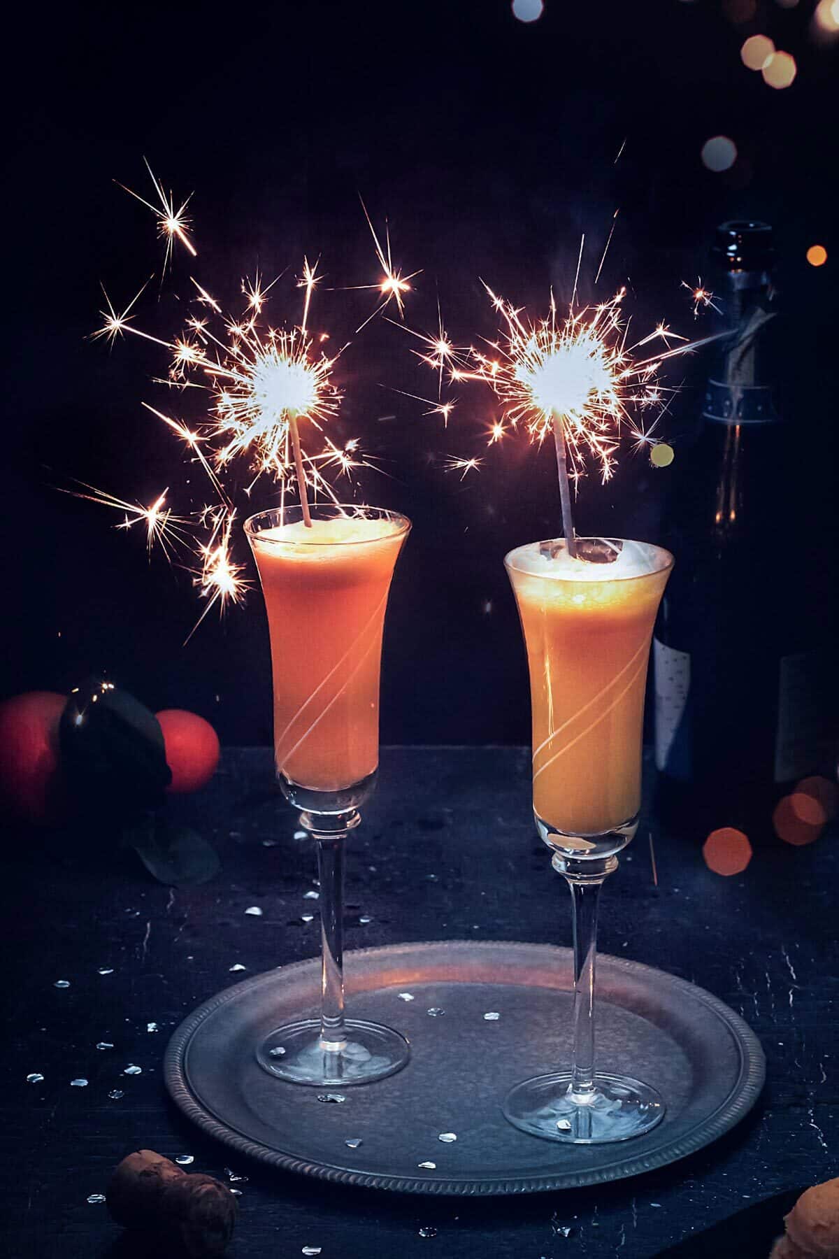 Two champagne flutes with mimosa cocktail and sparkles.