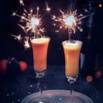 Two champagne flutes with mimosa cocktail and sparkles.