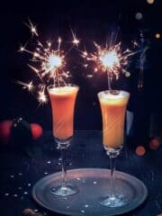 Two champagne flutes with mimosa cocktail and sparkles.