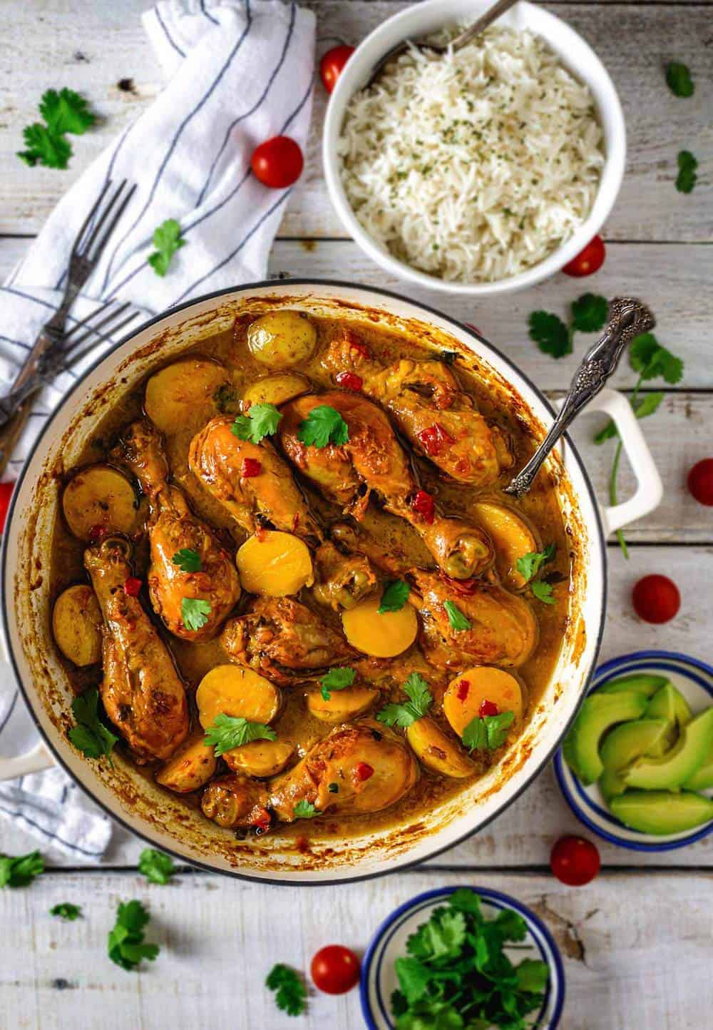 A Dutch oven with Colombian chicken and potato stew with rice and avocado servings on the table.