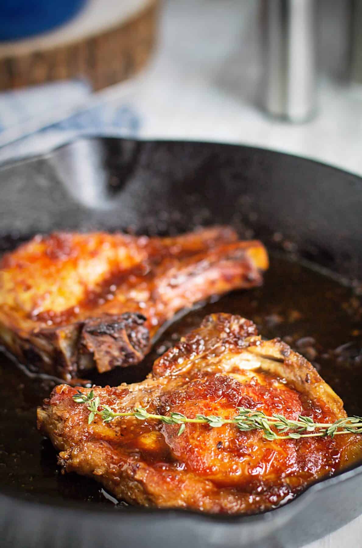 A close up of two baked pork chops in a cast-iron skillet.