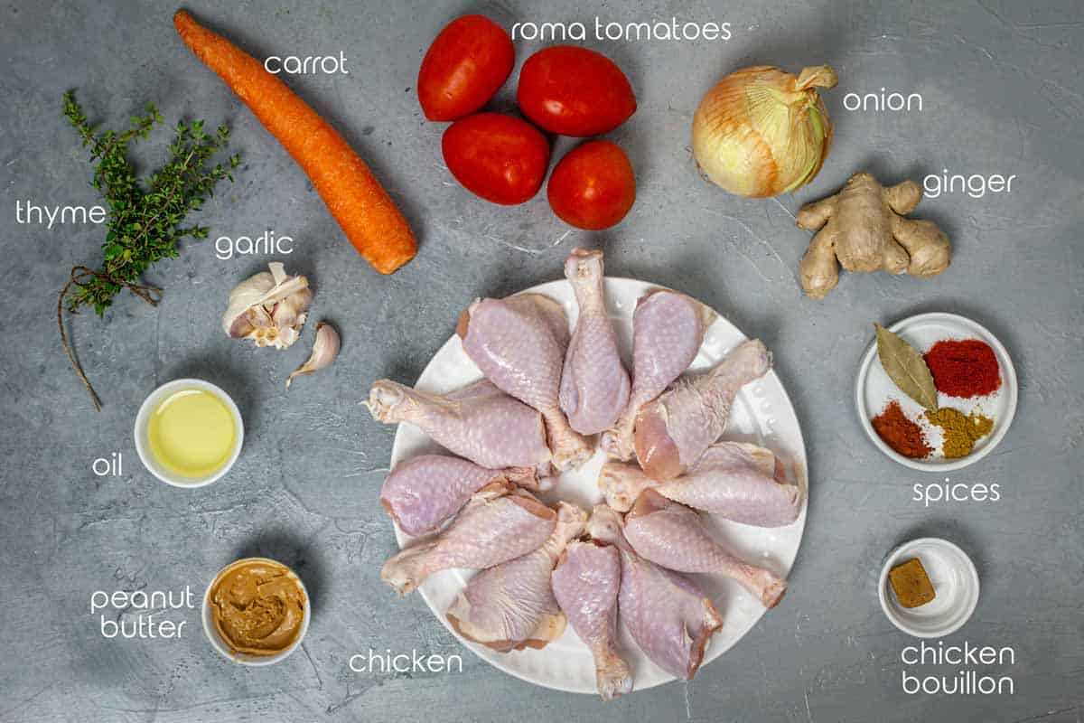 Ingredients for West African groundnut stew with chicken drumsticks, tomatoes, ginger, carrot, garlic, and onion.