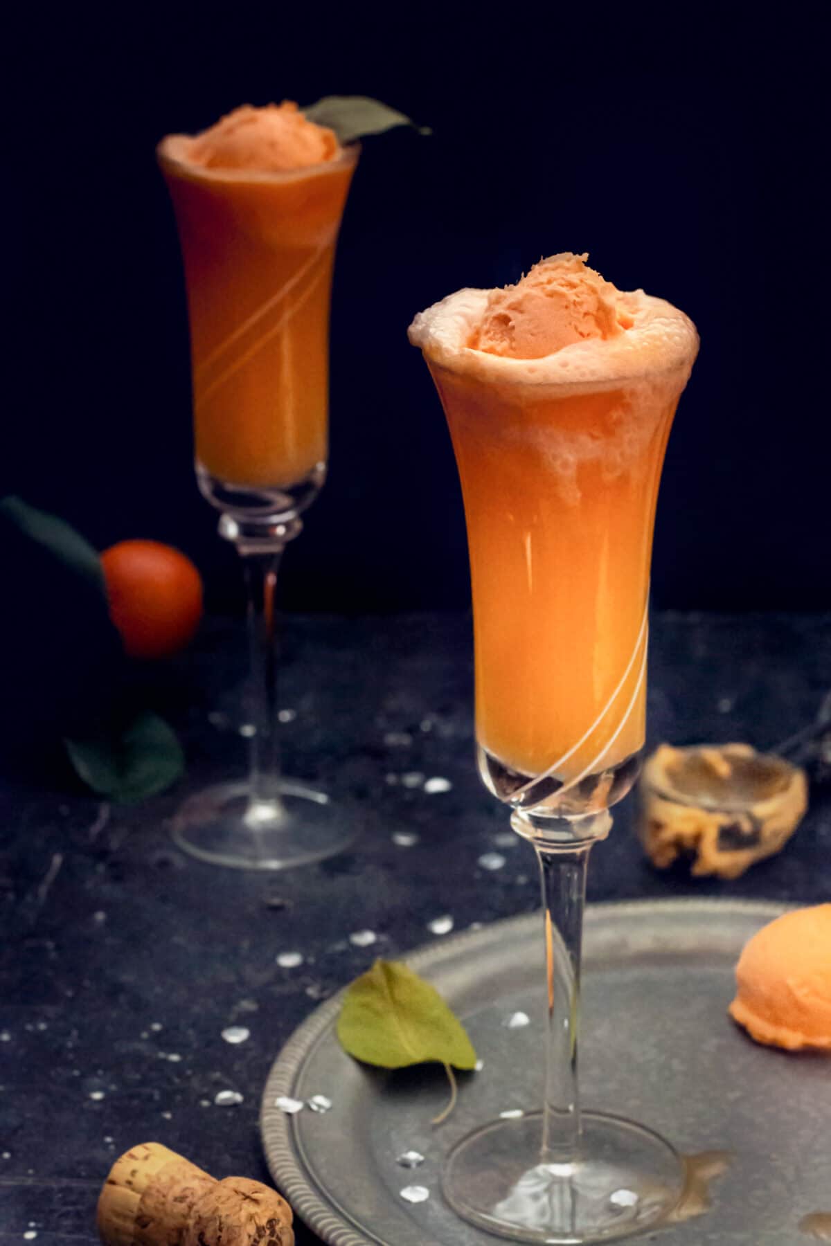 Two champagne glasses with orange sorbet mimosa drink.