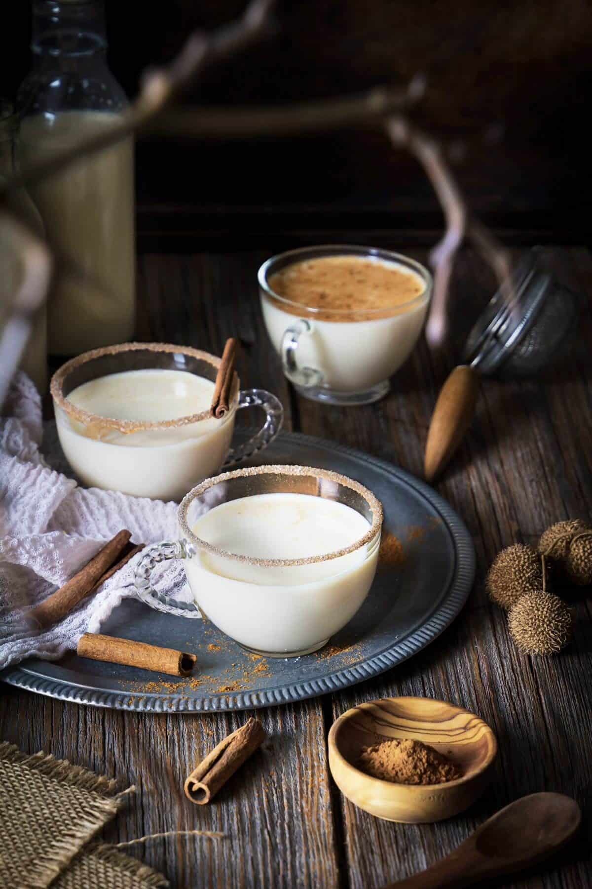 Three small glasses with milk tart cocktail on a rustic wooden table and cinnamon.