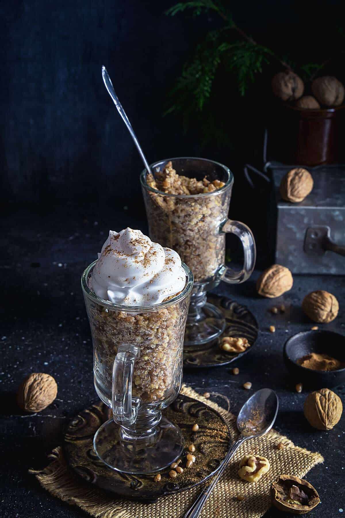 Two glasses with whole wheat berry pudding on a table, with walnuts and whipped cream.