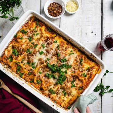 A person putting a white dish with lasagna on a rustic white table.