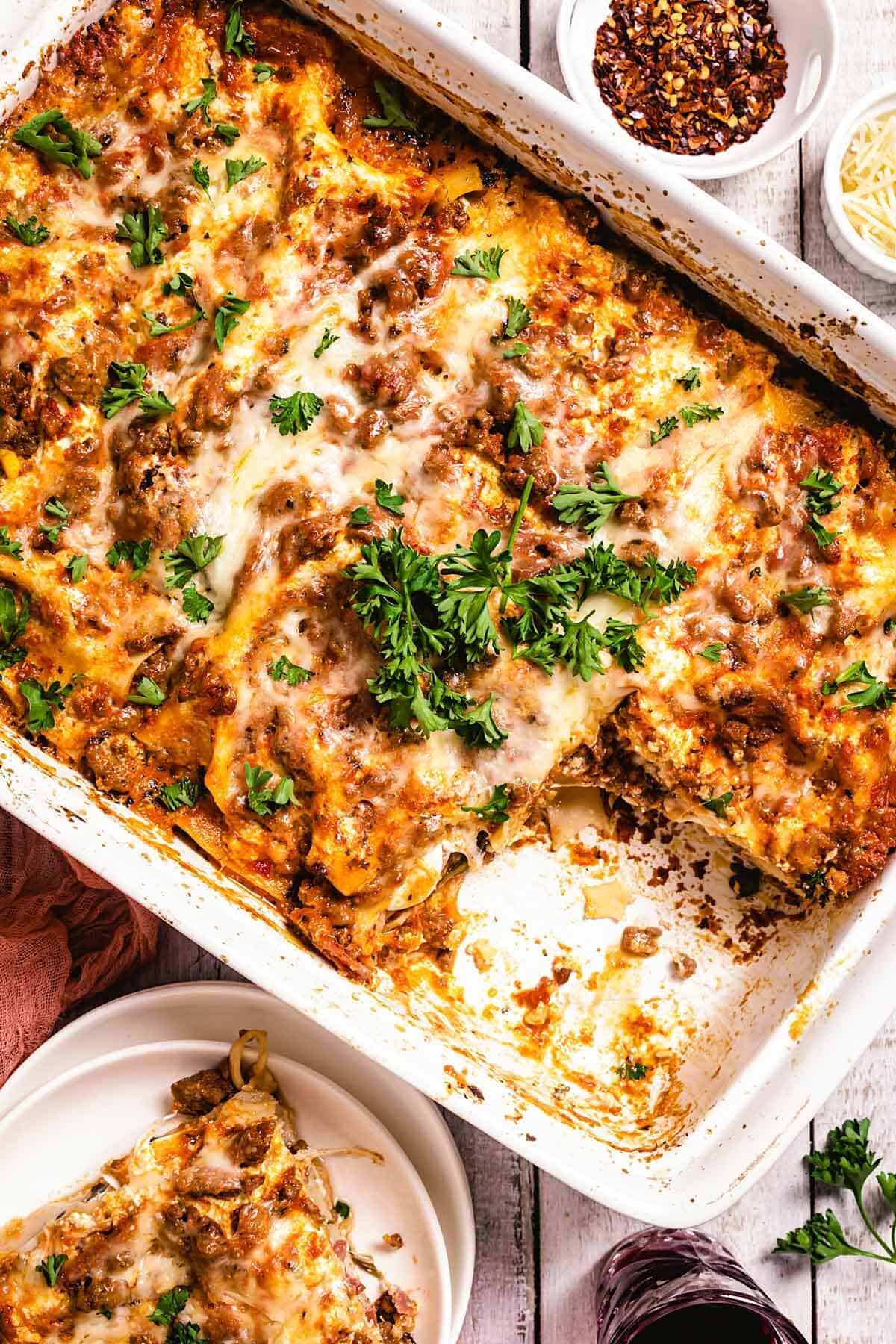 A pan with lasagna and parsley on a table with a plate.