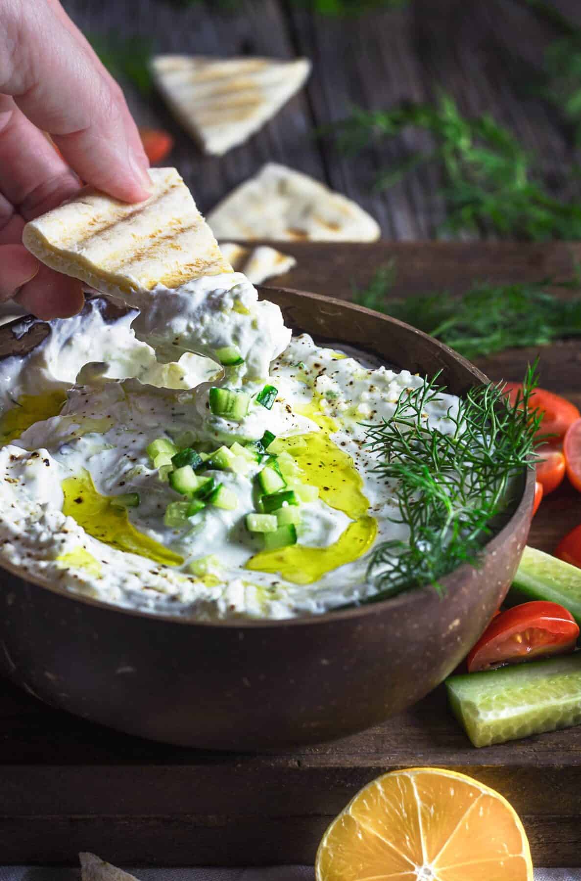 A person dipping pita wedge into the bowl with Greek dip.