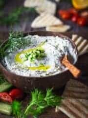 A wooden bowl with tzatziki sauce and wooden spoon, served with grilled pita bread wedges.