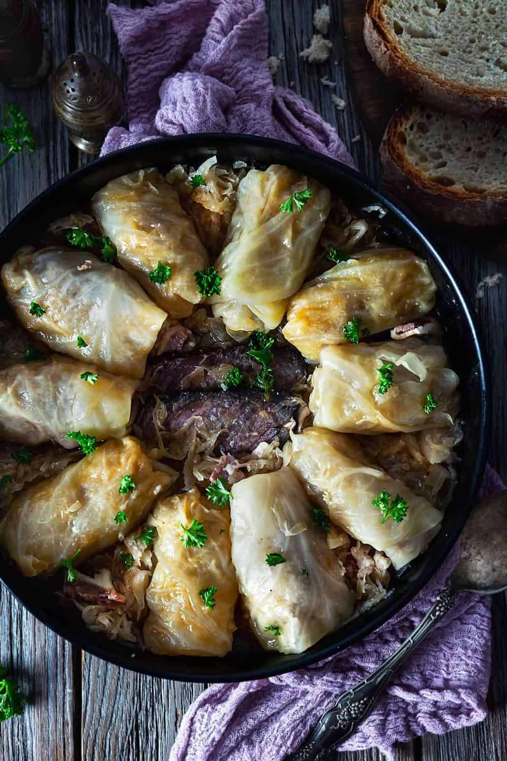 An overhead photo of cabbage rolls placed in a circle in a round dish with smoked meat in the middle.