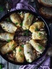An overhead photo of cabbage rolls placed in a circle in a round dish with smoked meat in the middle.