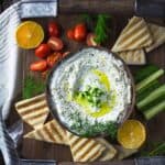 An overhead photo of yogurt dip with cucumber, dill, lemon, and garlic, served with vegetables and pita bread.